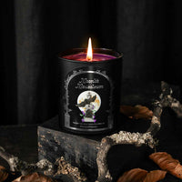 Thumbnail for A black candle jar labeled 'Moonlit Masqueum' with a lit purple wax surface and flame, styled on a dark textured block with dried leaves and branches against a black backdrop.